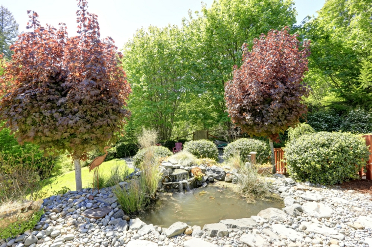 un estanque con esculturas rocas jardines arboles rodeado color